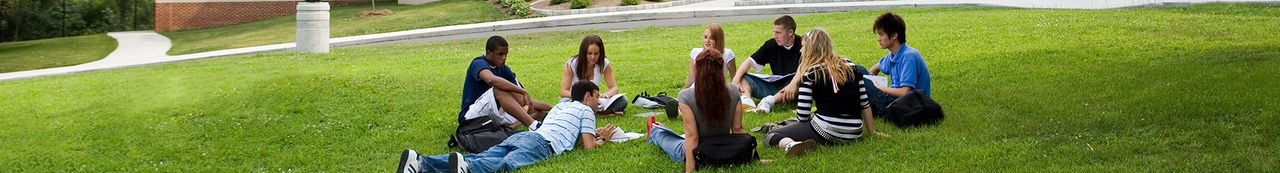 Students sitting together outside looking at a computer and smiling
