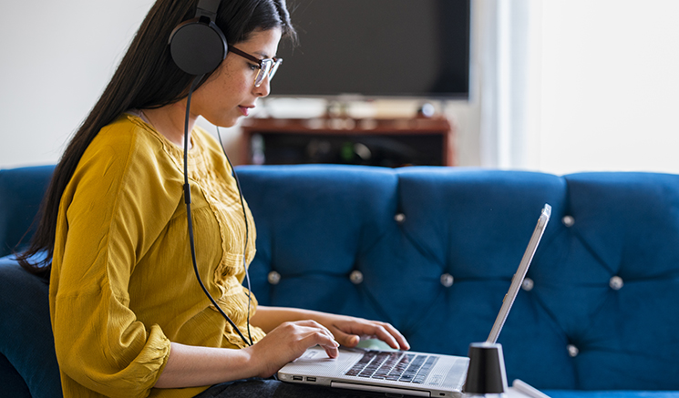Woman in a yellow shirt wearing headphones while using her laptop