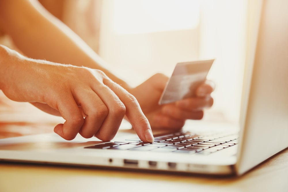 woman holds credit card in hand while using laptop